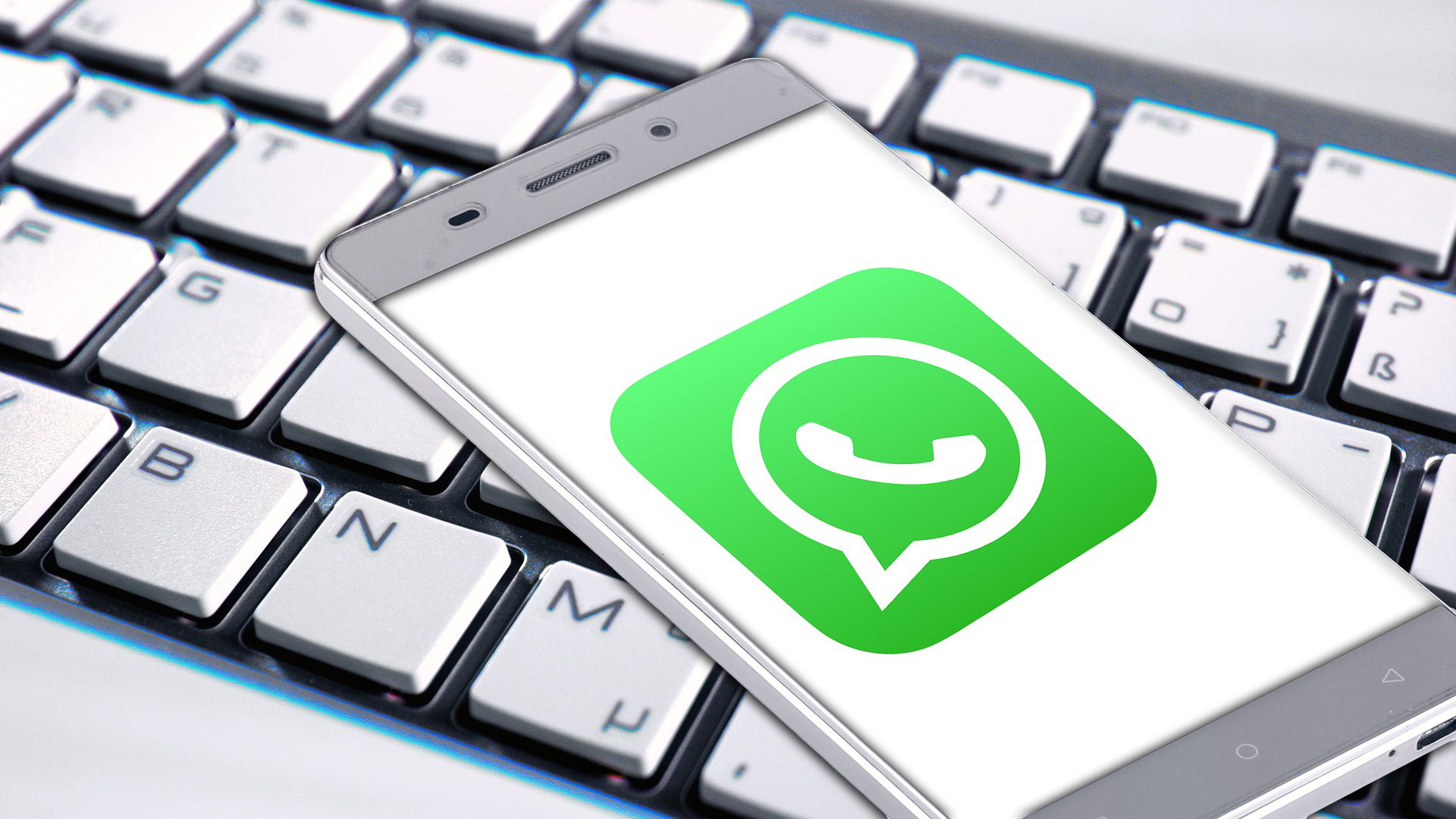 Ein Smartphone mit eingeblendetem WhatsApp-Icon liegt auf einer Computertastatur.